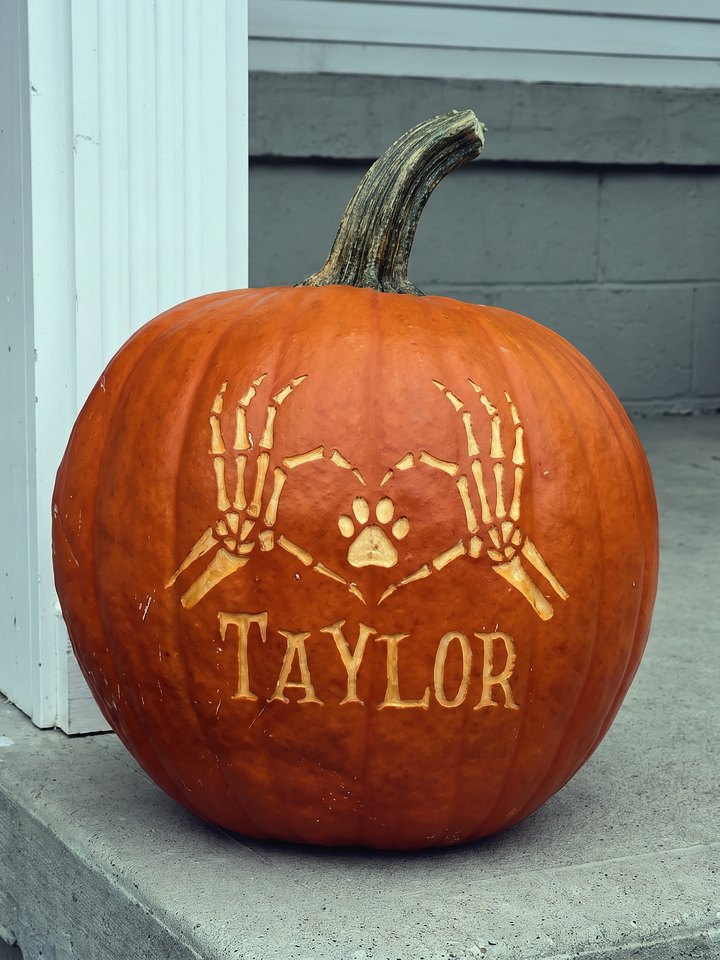 A pumpkin laser-engraved with skeleton hands, a paw print, and the name Taylor, on a porch