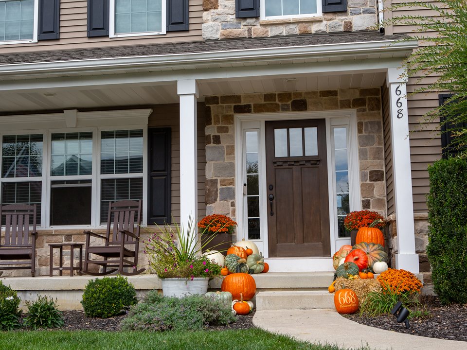 A front entrance with pumpkins in orange, white and sage green either side of the door, a mum on each side and a straw bale on the step