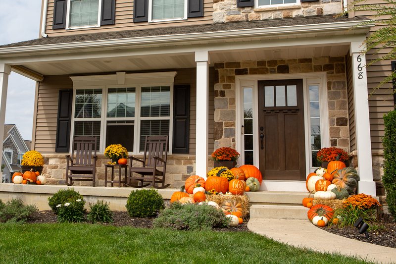 The Estate on a stone-front colonial: pumpkins running across the porch and down the steps on straw bales both sides, mums, white and sage green pumpkins and gourds, an engraved family-name pumpkin, a house number and a Mason pumpkin